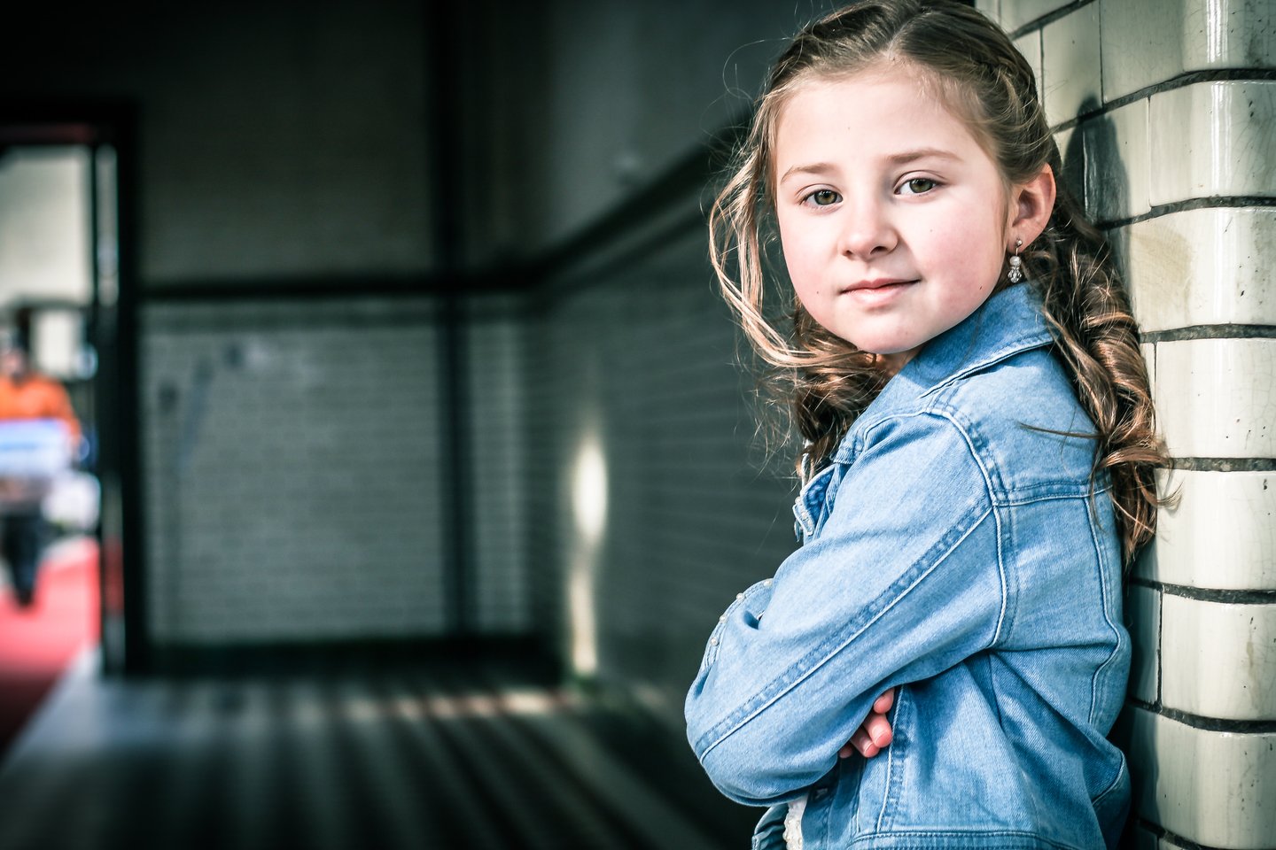 A child in a denim jacket standing beside a tiled wall